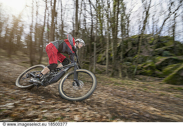 Mountain biker speeding downhill on e-bike through forest track  Bozen  Trentino  Italy