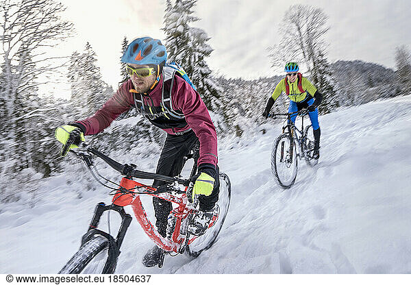 Mountain bikers in sportswear riding cycle in snow