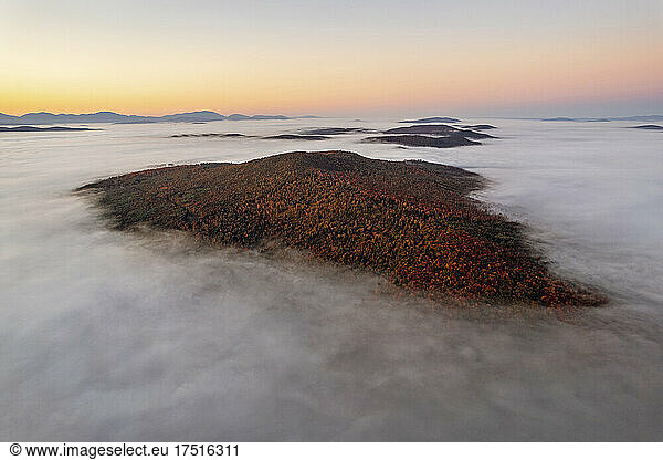 Mountain covered in fall foliage rises above mist  Vermont