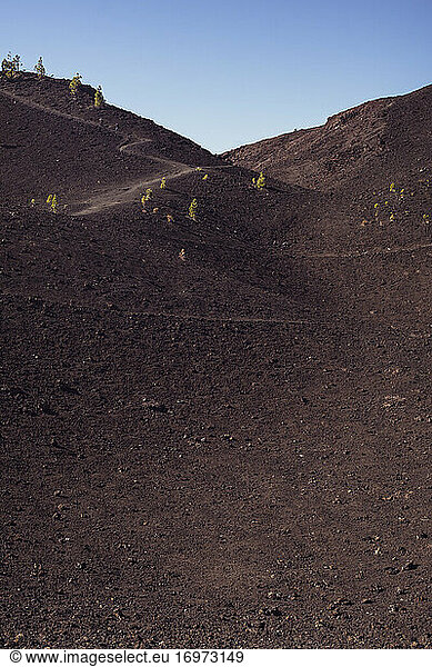 mountain path winds through dry brown volcanic soil with two hikers