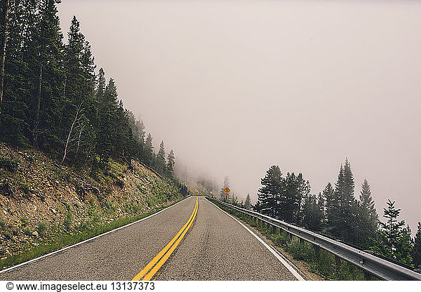 Mountain road amidst trees against sky in foggy weather
