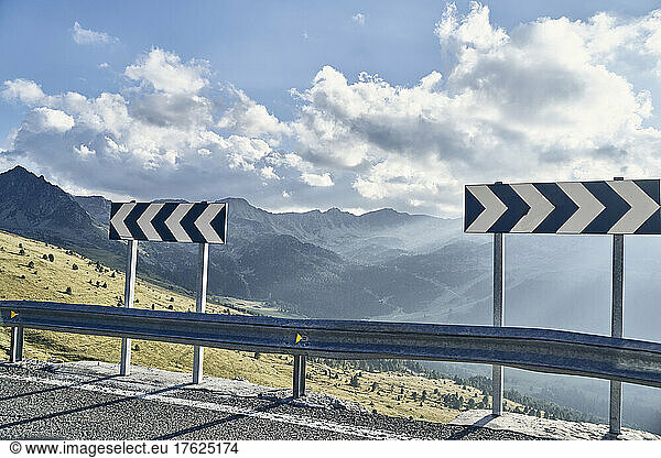 Mountain road with traffic arrow sign on sunny day