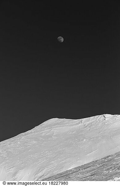 Mountain top covered in snow with the moon in the background