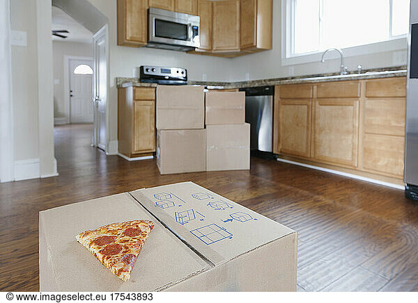 Moving house  relocation  cardboard boxes piled up in a house fitted kitchen  a slice of pizza.