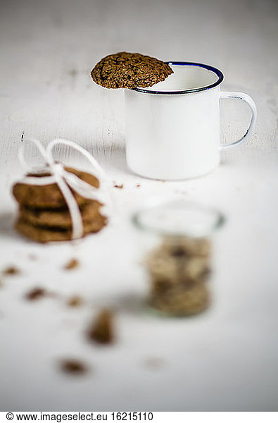 Mug with cookie on edge  stack of cookies with glass of walnuts  close up