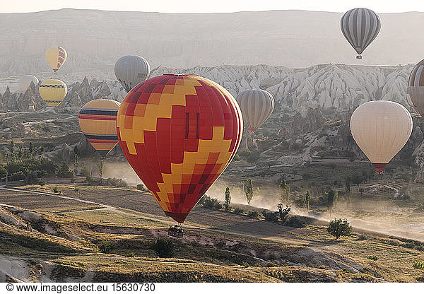 Multi colored hot air balloons flying over land at Goreme National Park during sunset  Cappadocia  Turkey