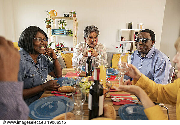 Multi-cultural senior friends having dinner at dining table in home