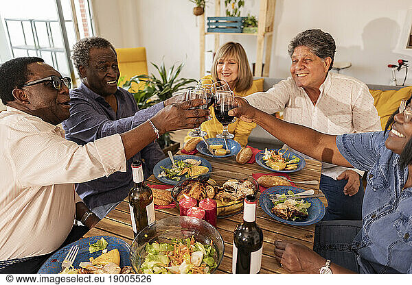 Multi-cultural senior friends toasting wineglasses sitting at dining table