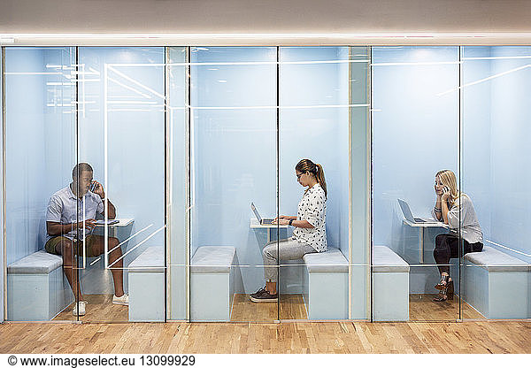 Multi-ethnic business people using laptops while sitting in cubicles at office