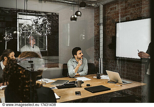 Multi-ethnic business professional looking at male entrepreneur giving presentation in broad room
