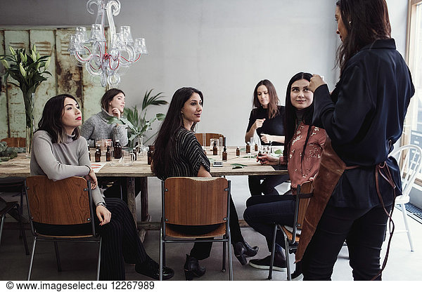 Multi-ethnic female colleagues looking at mid adult owner standing in perfume workshop