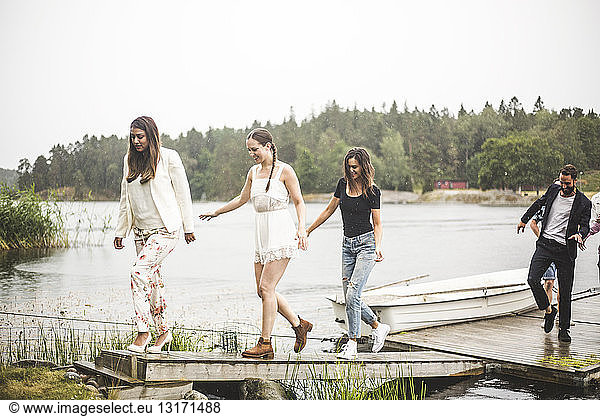 Multi-ethnic friends walking on jetty over lake during weekend getaway