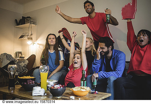 Multi-ethnic friends watching sport while sitting on sofa at home