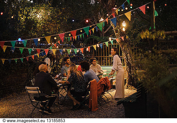 Multi-ethnic male and female friends enjoying dinner party in illuminated backyard