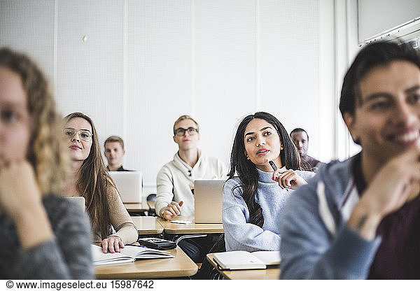 Multi-ethnic male and female students sitting at desk in classroom