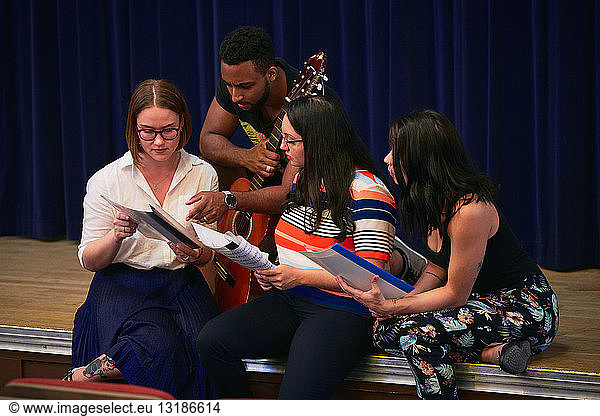 Multi-ethnic students reading music sheets on stage in auditorium