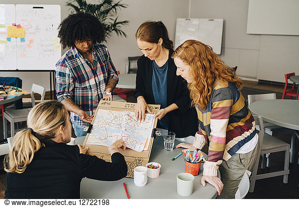 Multi-ethnic students showing map on placard to female manager at table in creative office