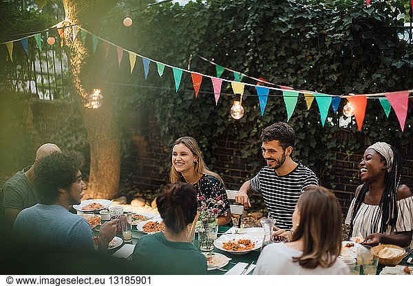 Multi-ethnic young friends enjoying dinner at table during garden party