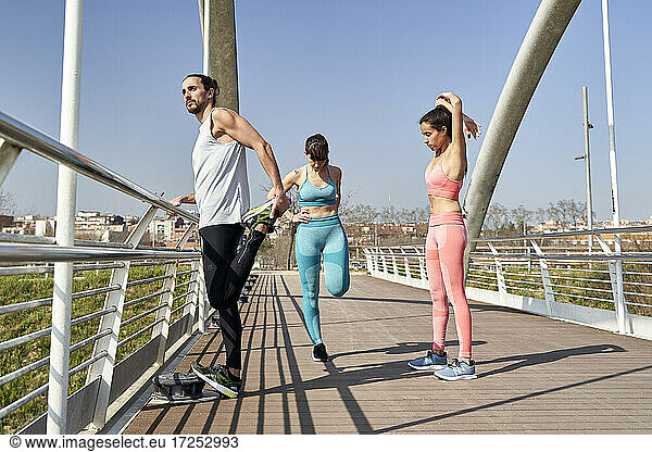 Multi-ethnische männliche und weibliche Athleten bei Übungen auf einer Brücke an einem sonnigen Tag
