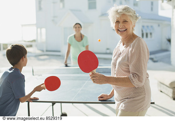 Multi-generation family playing table tennis outside beach house