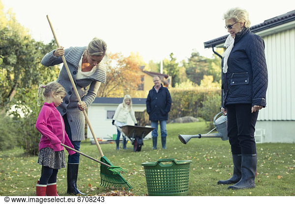 Multi-generation family raking autumn leaves at yard