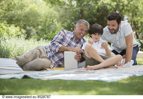 Multi-generation men with cell phone on blanket in grass