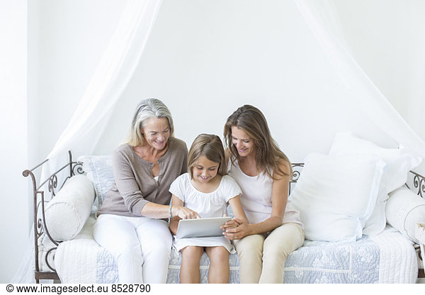 Multi-generation women using digital tablet on daybed