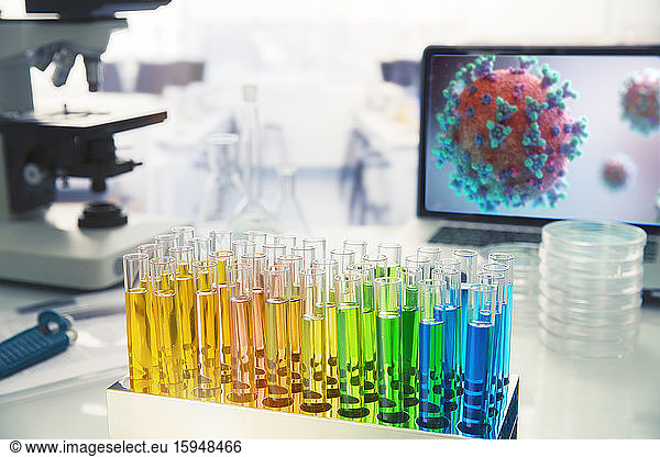 Multicolor vials on laboratory table next to coronavirus on screen