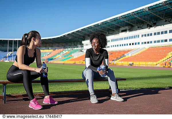 Multiethnic sportswomen resting on bench together
