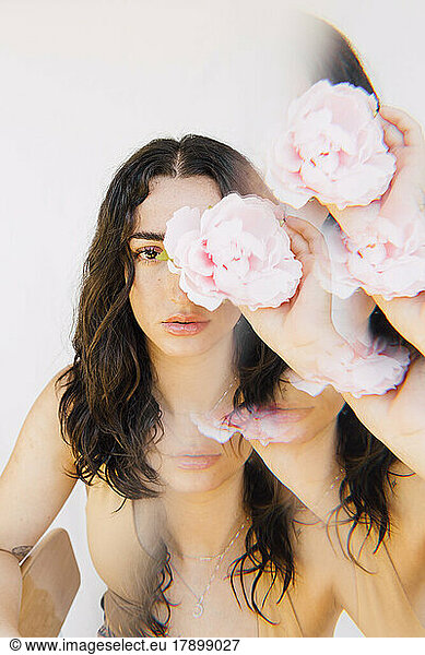 Multiple exposure of young woman holding pink flower over eye