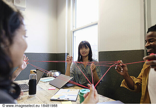 Multiracial business colleagues playing cat's cradle in break time at workplace