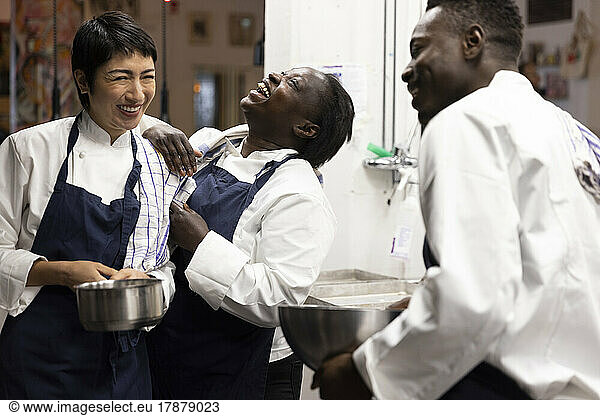 Multiracial chefs laughing while working in kitchen of restaurant