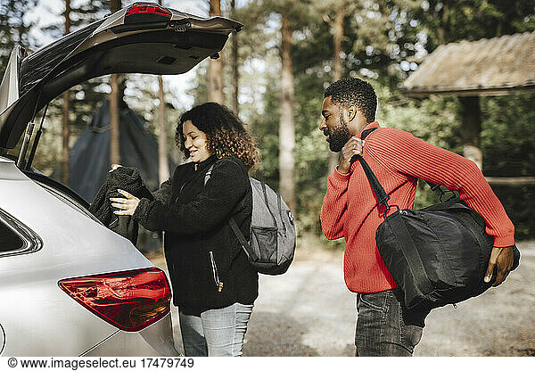 Multiracial couple loading luggage in car trunk during vacation