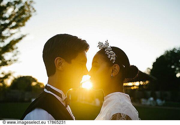 Multiracial couple touch noses in loving embrace with sunset
