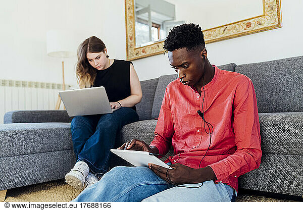 Multiracial couple using laptop and tablet PC in living room at home