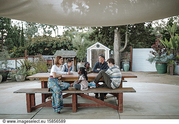 Multiracial family gathered at picnic table under sunshade at nursery