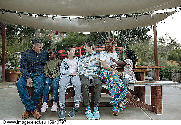Multiracial family relaxing on a bench under a white sun canopy
