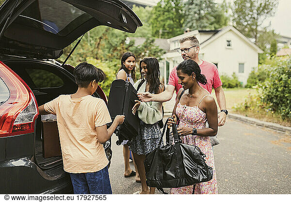 Multiracial family unloading luggage from car trunk while standing on road