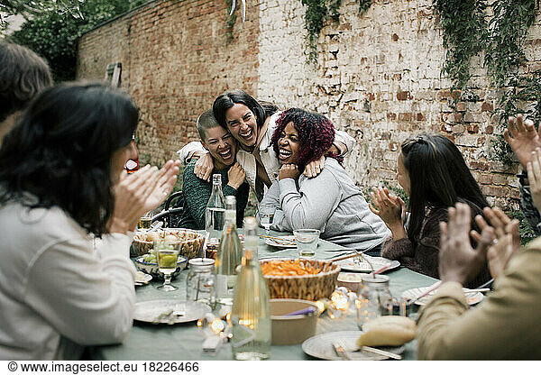 Multiracial female friends laughing together during dinner party in back yard