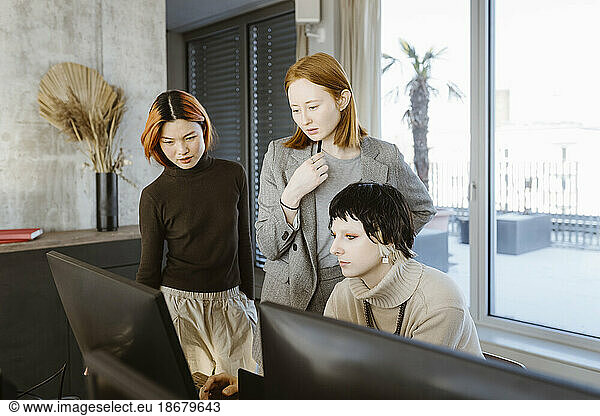 Multiracial female programmers discussing over computer at desk in startup office