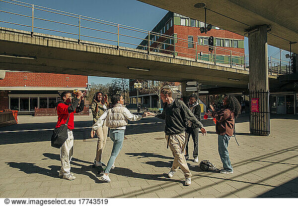 Multiracial friends applauding at young man and woman dancing at street on sunny day