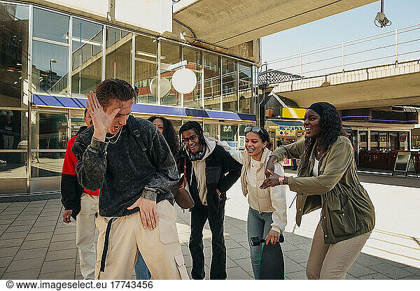 Multiracial friends cheering young man dancing at street