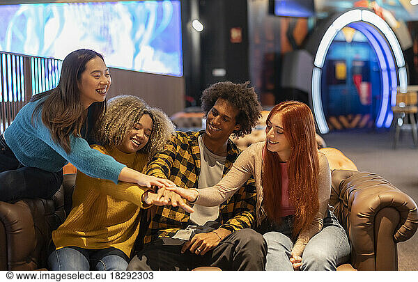 Multiracial friends stacking hands in bowling alley