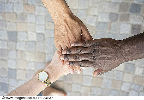 Multiracial friends stacking hands over footpath