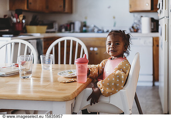 Multiracial girl with sippie cup wearing bib in high chair