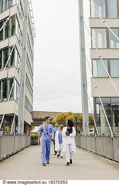 Multiracial group of male and female healthcare staff walking on bridge amidst hospital building