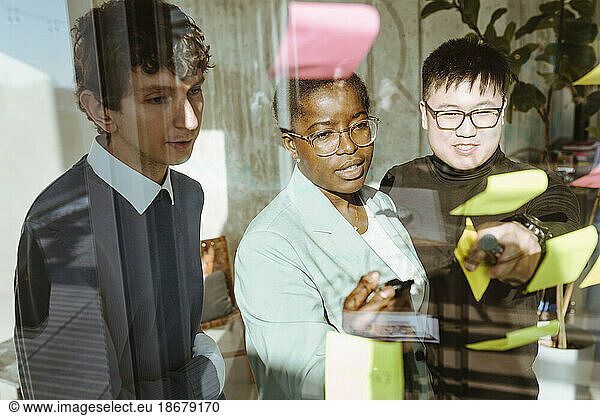 Multiracial male and female colleagues discussing over sticky notes in creative office