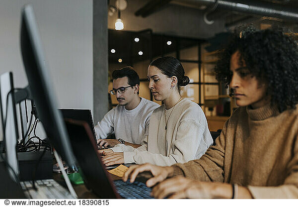 Multiracial male and female hackers working on laptop at creative workplace