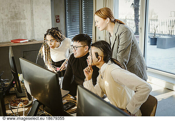 Multiracial male and female programmers discussing over computer in creative office