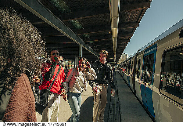 Multiracial playful friends standing near train at railroad station